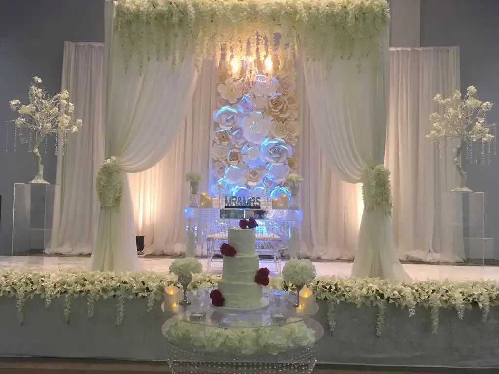 All-white floral reception stage with red rose wedding cake · Dream Decorators