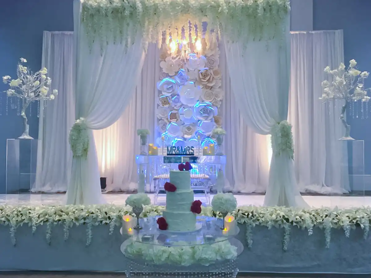 White floral wall reception stage with wedding cake · Dream Decorators
