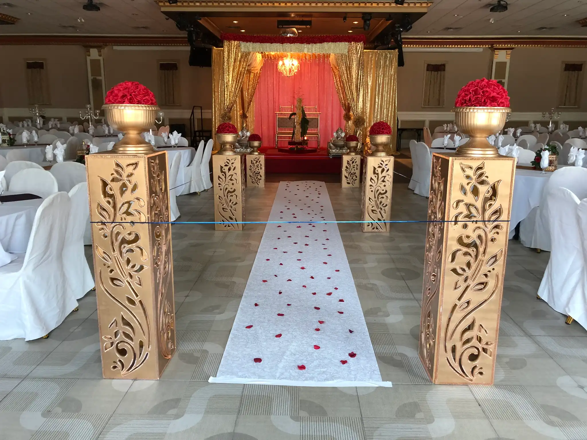 Gold mandap aisle with red rose pillars and thrones · Dream Decorators