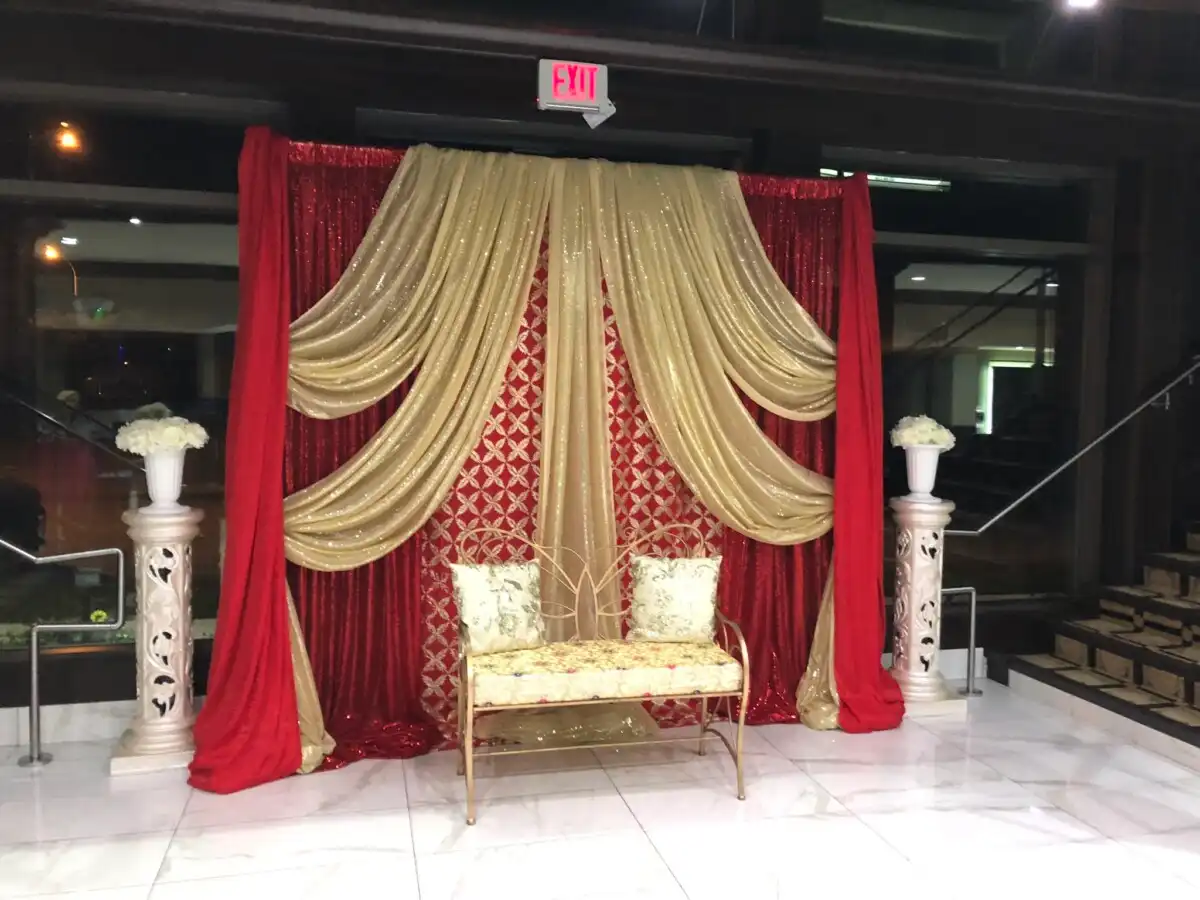 Red and gold patterned wedding backdrop with gold bench · Dream Decorators