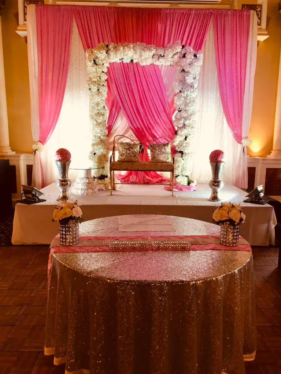 Pink floral arch reception stage with gold loveseat · Dream Decorators