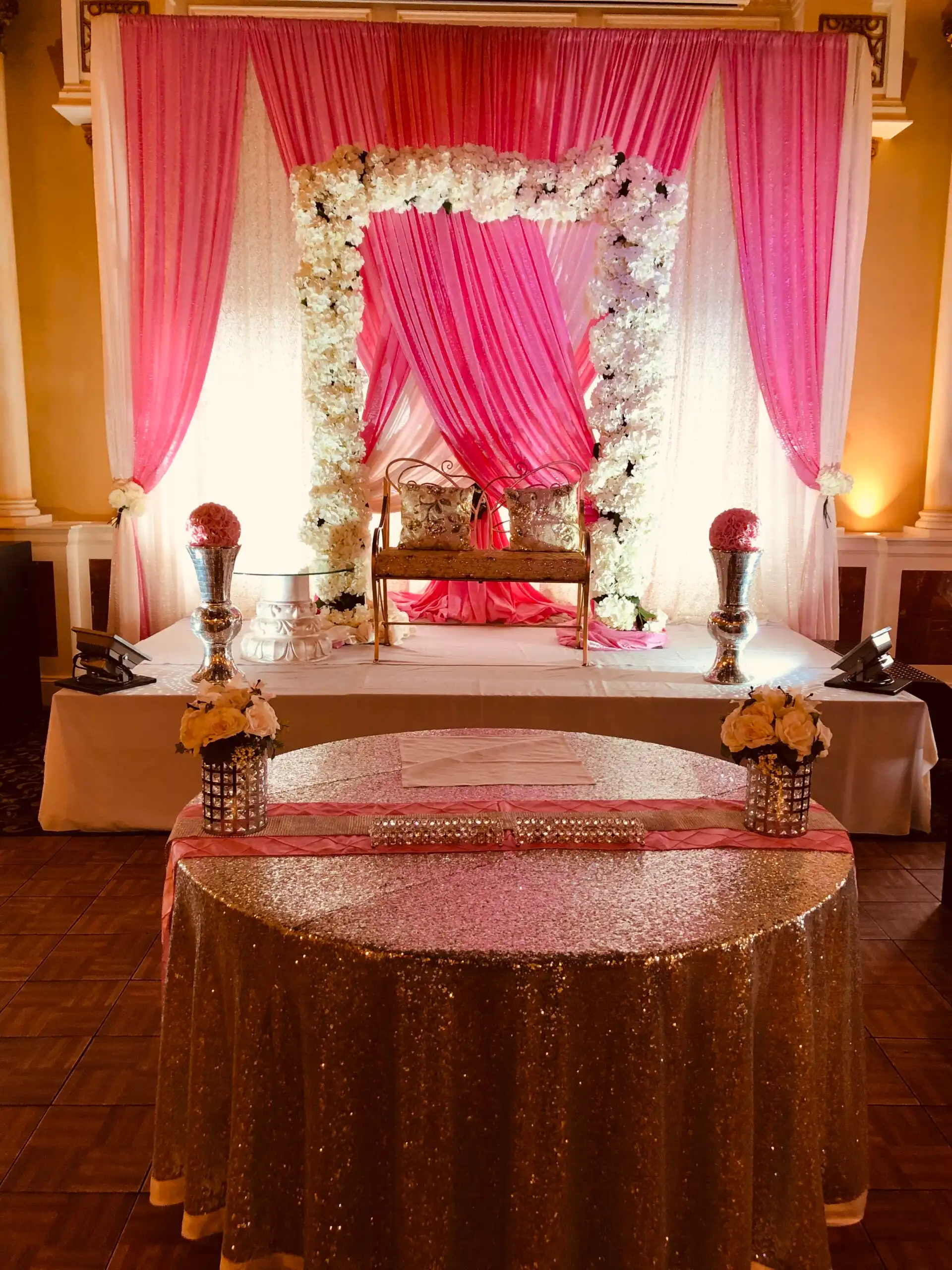 Pink floral arch reception stage with gold bench · Dream Decorators