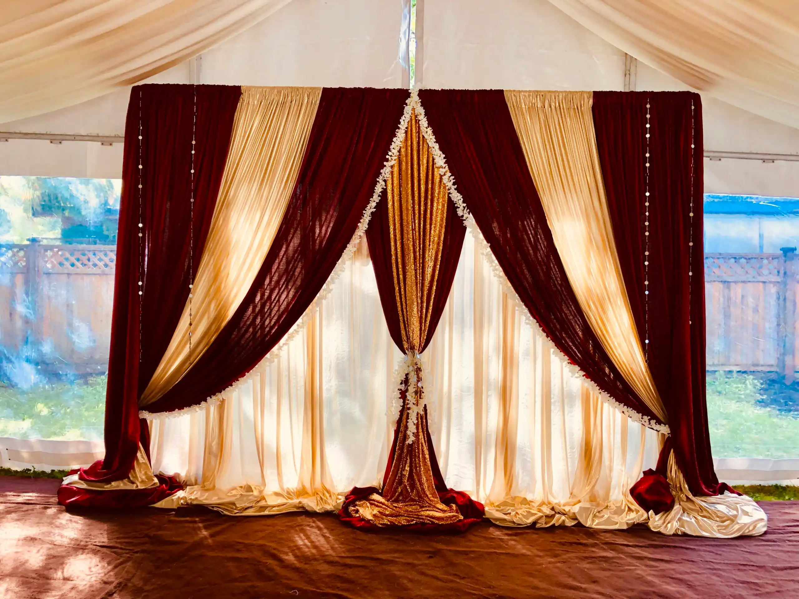 Burgundy and gold draped backdrop in backyard tent · Dream Decorators