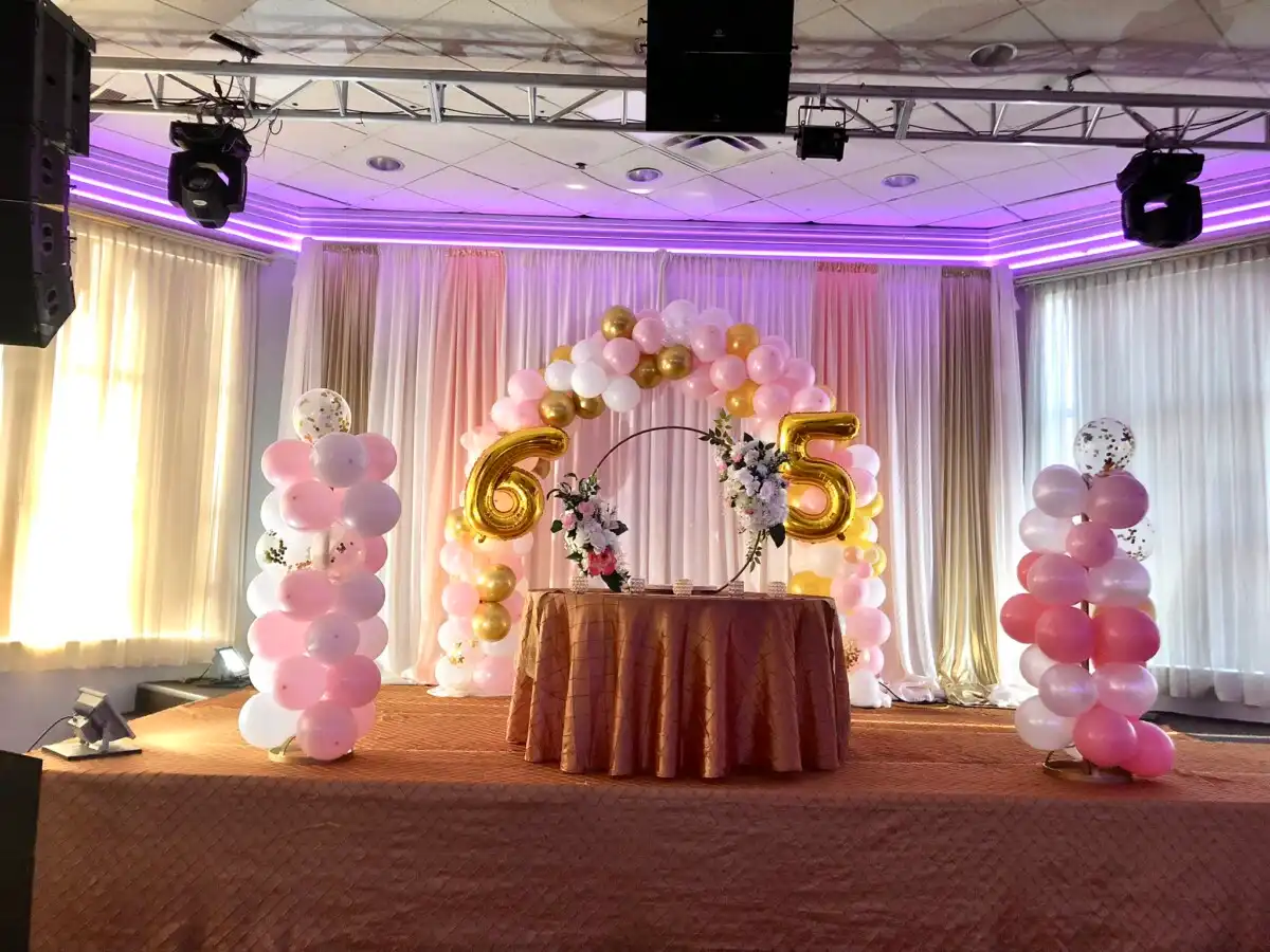 Pink and gold 65th birthday stage with balloon arch · Dream Decorators