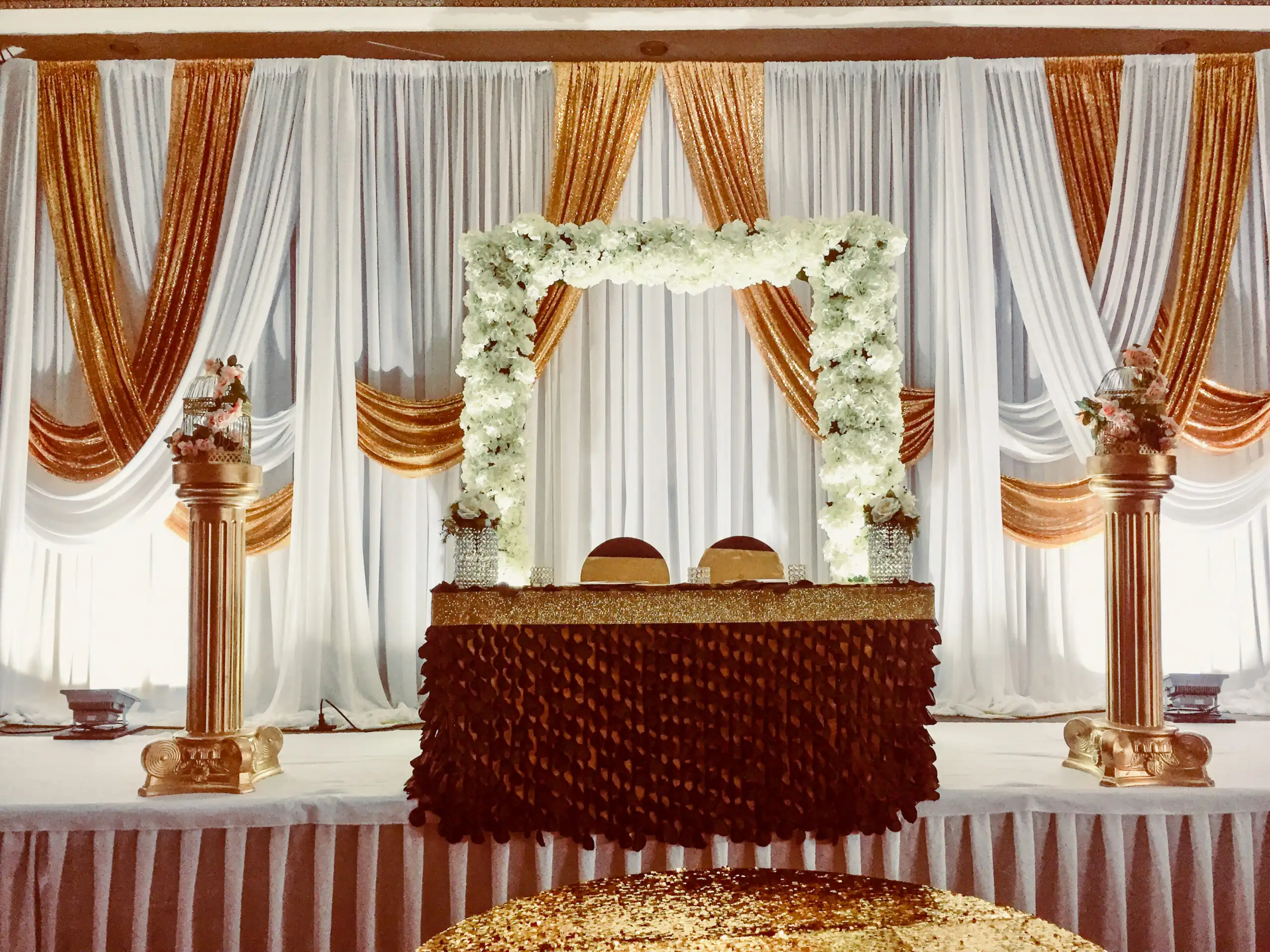 White floral arch reception stage with burgundy sweetheart table · Dream Decorators
